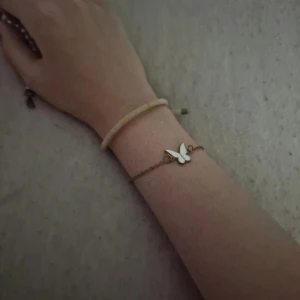 Armband med fjärilsberlock - Säljer ett sött armband med en liten fjärilsberlock. Armbandet har en tunn kedja i guld och fjärilen är vit. Perfekt för att lägga till en subtil touch av elegans till din outfit. Passar både till vardags och fest!