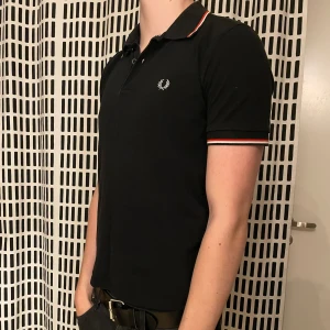 Fred perry piké  - Svart fred Perry piké i storlek S. Den är i bra skick förutom att lite av sömmen i botten har gått upp, men det går enkelt att sy igen. Jag på bilden är 185 och väger 70 och den sitter för kort på mig. Kontakta mig för frågor. Pris kan diskuteras 😁👍
