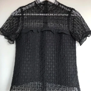 Svart spetsblus med volangdetaljer - Säljer en elegant svart spetsblus med korta ärmar och fina volangdetaljer. Perfekt för en festlig kväll eller en stilren vardagslook. Blusen har en vacker genombruten spetsdesign som ger en lyxig känsla.