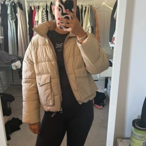 Beige pufferjacka från NA-KD - Säljer en snygg beige pufferjacka från NA-KD i storlek S. Jackan har en dragkedja framtill och stora fickor med knappar. Perfekt för kommande månader och ger en trendig look. Den är i bra skick och redo för en ny ägare!