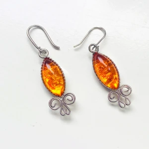 Silverörhängen med orange sten - Säljer ett par snygga vintage örhängen med en stor, oval orange rhinestone. Stenen har en vacker, skimrande yta och örhängena har en unik design med dekorativa detaljer i silver under stenen. Perfekta för att ge en färgklick till din outfit! Okänt material 