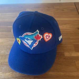 New era keps - Blå new era keps med Toronto och hjärtan. Strl 7 1/2 (59.6cm). Använd fåtal gånger, nypris runt 700-750
