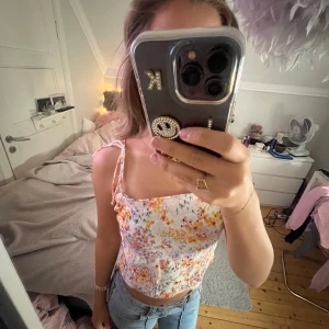 somrig topp - en super söt kortare topp med blommor och knyte vid axlarna 🧡 perfekt till sommaren!! storlek M men passar mig som är en storlek XS/S då man kan ändra längd på banden. Använd en gång. Original pris: 199kr
