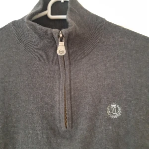 Grå tröja med dragkedja från Henri Lloyd - Säljer en snygg och stilren grå half zip tröja från Henri Lloyd. Den har en praktisk dragkedja framtill och ett broderat emblem på bröstet. Perfekt för både vardag och lite finare tillfällen. Tröjan är i nyskick och har aldrig använts. Passar perfekt till höst och vinter!
