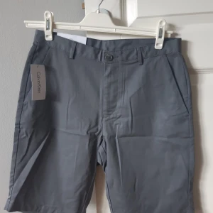 Grå shorts från Calvin Klein - Säljer ett par stilrena grå shorts från Calvin Klein. De är helt nya och har en klassisk design med fickor både fram och bak. Perfekta för sommarens alla tillfällen! Fått de i present så vet inte vad det är för kvalité/var de är inköpta. Helt nya med prislapp men för små för mig tyvärr. Normala i storleken.