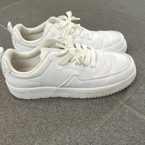 Vita sneakers med snörning - Säljer ett par vita sneakers i syntetmaterial. De har en klassisk design med snörning och en bekväm sula. Perfekta för vardagsbruk och passar till det mesta i garderoben.