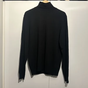 Svart polotröja från J.Lindeberg - Säljer en stilren svart polotröja från J.Lindeberg. Den är perfekt för både höst och vinter med sin klassiska design och långa ärmar. Tröjan är i bra skick och passar till många olika outfits. Perfekt för dig som vill ha något enkelt men snyggt i garderoben!