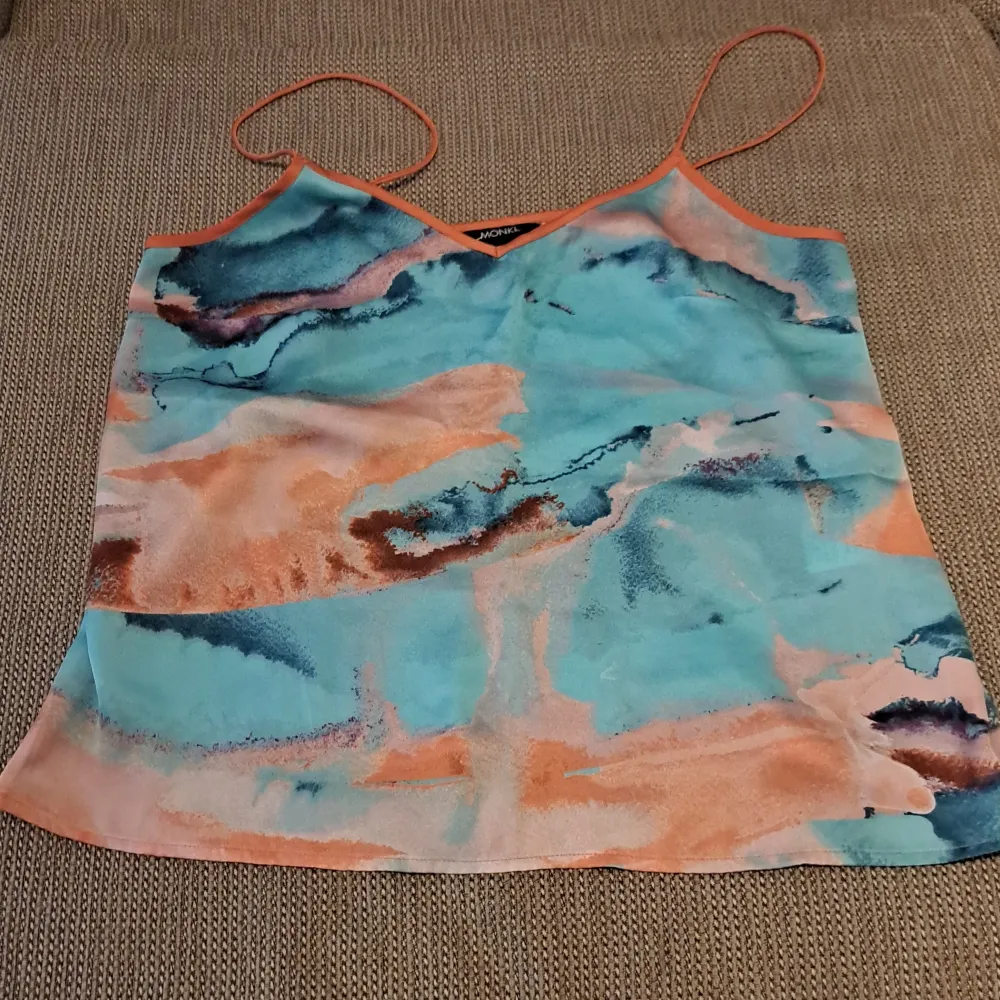 Säljer en superfin linne topp med ett abstrakt mönster i blått, orange och beige. Toppen har tunna axelband och en v-ringad halslinje. Perfekt för sommardagar eller en festlig kväll! . Yläosat.