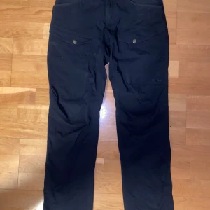 Svarta byxor från Haglöfs - Säljer ett par svarta byxor från Haglöfs med praktiska fickor och knappar. Perfekta för utomhusaktiviteter med en robust design.