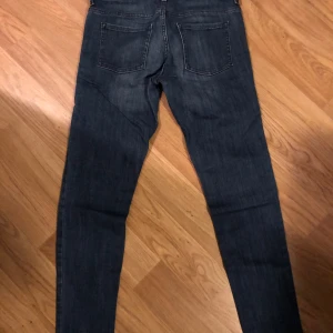 Mörkblå jeans HM  med detaljer - Snygga mörkblå jeans med unika sömdetaljer på framsidan. De har en klassisk femficksdesign och en smal passform som ger en modern look. Perfekta för en stilren vardagsoutfit.