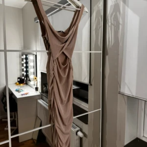 Beige omlottklänning - Elegant beige omlottklänning med draperad design. Klänningen har en smickrande passform och är perfekt för speciella tillfällen.
