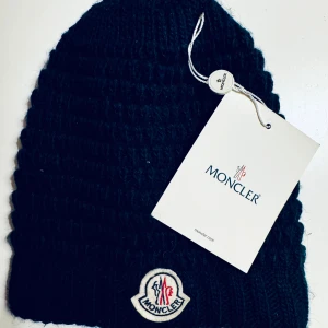 Moncler - oanvänd mössa - Tidlöst marinblå stickad mössa från Moncler med broderad logotyp. Perfekt för såväl vinter som vår. Givetvis äkta och kommer med patch.