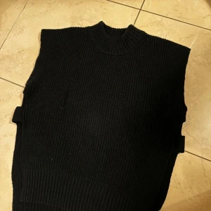 Svart stickad väst från Gina Tricot - Snygg svart stickad väst från Gina Tricot i storlek M. Perfekt för lager-på-lager-stil med ribbad design och rund halsringning. 