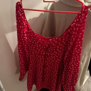 Röd blommig klänning - Charmig röd klänning med små vita blommor och v-ringad design. Klänningen har långa ärmar och en smickrande passform. Perfekt för vår och sommar!