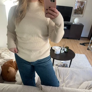 Beige ribbad tröja - Säljer en stilren beige ribbad tröja med långa ärmar. Perfekt för en avslappnad look och passar bra till jeans. Tröjan har en klassisk design med högre krage.
