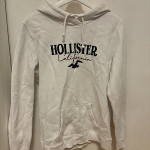 Vit hoodie från Hollister - Säljer en snygga vit hoodie från Hollister. Tröjan har en klassisk känguruficka och justerbar huva med dragsko. Perfekt för en avslappnad stil.