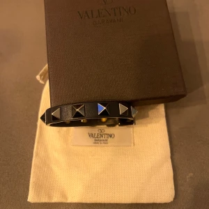 Valentino armband  - Snyggt mörkblått armband från Valentino Garavani.  Armbandet har en justerbar knäppning och kommer i originalförpackning med dustbag. Defekt på spännet i bild 3, defekten är inget som märks av när man har på sig armbandet och syns knappt eftersom spännet sitter på undersidan av handleden. Tveka inte på att höra av sig vid frågor!😊 