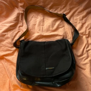 Svart axelväska från samsonite - Säljer en praktisk svart axelväska från Samsonite. Väskan har ett rymligt huvudfack med plats för en laptop, samt flera innerfickor för enkel organisering. Den justerbara axelremmen gör den bekväm att bära. Perfekt för både arbete och studier.