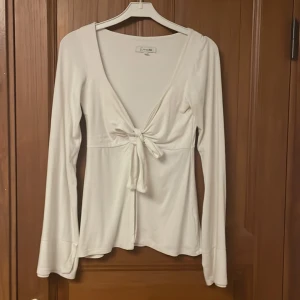 Vit långärmad topp från design by si - Säljer en stilren vit långärmad topp från design by si med knytning framtill. Toppen har en djup v-ringning och är perfekt för fester. Passar bra till både jeans och kjol. Den är i dubbel storlek xs/s å är i ett mjukt material så den passar båda💕