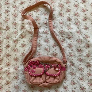 Rosa liten väska från Hushush Japan - Söt rosa axelväska med prickiga och hjärtformade detaljer. Väskan har två små fickor framtill och en dragkedja upptill. Köpt från Japan och troligen till för barn/tonåringar. Aldrig använd av mig, bra skick! 