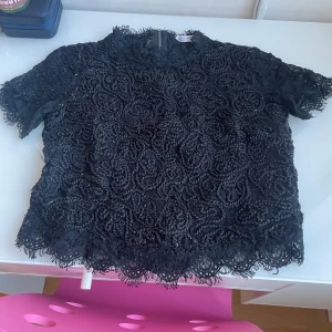Svart spetsblus från Zara - Snygg svart spetsblus från Zara med korta ärmar och ett vackert mönster. Perfekt för att ge en elegant touch till din outfit. Blusen har en fin struktur och är lätt att matcha med olika stilar.