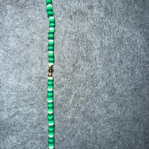 Grönt armband med pärlor - Snyggt armband med gröna och vita platta pärlor. Armbandet har en enkel och stilren design med ett diskret lås i metall. Perfekt för att ge en färgklick till din outfit.