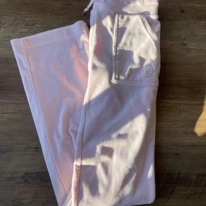 Rosa mjukisbyxor från Juicy Couture - Säljer ett par rosa mjukisbyxor från Juicy Couture. Byxorna har en bekväm passform med elastisk midja och snörning. De har praktiska fickor både fram och bak med knapplås.