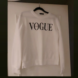Vit sweatshirt med Vogue-tryck - Snygg vit sweatshirt med stort Vogue-tryck på framsidan. Tröjan har en klassisk rund hals och långa ärmar, perfekt för en stilren look. Passar bra till både jeans och kjol.