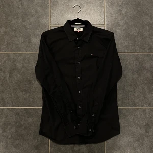 Svart skjorta från Tommy Jeans - Snygg svart skjorta från Tommy Jeans i storlek M. Skjortan har långa ärmar och knappar framtill. Perfekt för en stilren look.