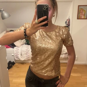 Guldig glitter paljettopp  - Den perfekta festtoppen! Super bra skick, med en dragskedja vid sidan så att du själv kan välja om du vill dra ner hela eller inte beroende på hur tajt du vill att den ska sitta.  Pris kan diskuteras vid snabb affär. Finns fler lågmidjade jeans, trendiga tröjor och väskor billigt i min profil!