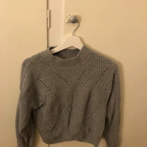 Grå stickad tröja från H&M - Säljer en stilren grå stickad tröja från H&M. Tröjan har ett diskret mönster och ribbstickade detaljer vid hals och ärmslut. Perfekt för kyligare dagar!