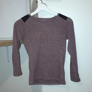 Långärmad tröja med svarta axeldetaljer - Säljer en snygg långärmad tröja i en dämpad lila nyans med coola svarta axeldetaljer/gjort av skinn. Perfekt för barn i åldern 9-10 år. Tröjan har en bekväm passform och är idealisk för både skola och fritid. Jättebekväm då den har ett väldigt mjukt material.