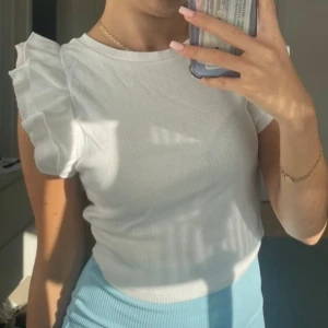 Vit ribbad topp med volangärmar - Säljer en söt vit ribbad topp med volangdetaljer på ärmarna. Köpt från zara.