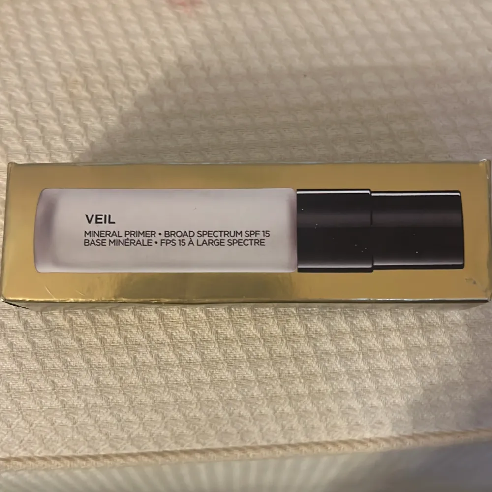 Säljer en Veil Mineral Primer från Hourglass med bredspektrum SPF 15. Denna primer är perfekt för att skapa en jämn bas och skydda huden mot solen. Förpackningen är elegant med en vit och svart design och innehåller 8,9 ml.. Beauty.
