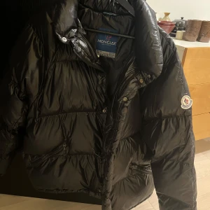 Svart dunjacka från Moncler - Säljer en svart vintage pufferjacka från Moncler som har en glansig finish och stängs med dragkedja och knappar. Stor för mig som vanligtvis bär XXS och är 160. Som ny, endast etiketterna inuti har blivit lite färgade efter användning