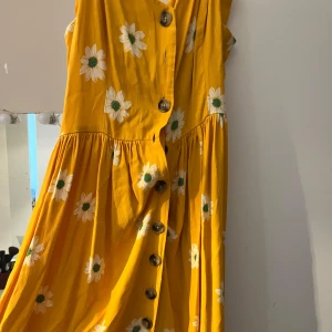 Gul blommig klänning med knappar från Mavi - Charmig gul klänning med vita blommor och knappar framtill. Perfekt för soliga dagar med sin lätta och luftiga design.