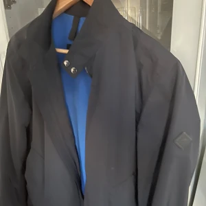 J Lindeberg derek jkt  - Snygg marinblå med dragkedja och knappar. Perfekt för en stilren look. Jackan har korta ärmar och en klassisk design.