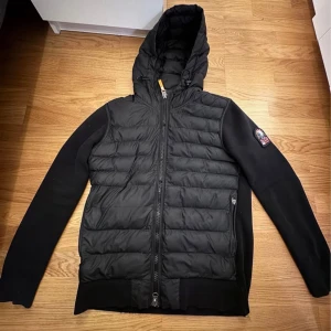 Parajumper Cardigan - Snygg svart jacka från PJS med huva och dragkedja. Jackan har en quiltad framsida och ribbade muddar. Perfekt för kyligare dagar.