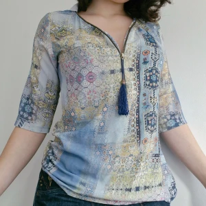 Mönstrad blus från MGC Collection - Säljer en färgglad blus från MGC Collection med ett unikt mönster i blått, gult och rosa. Blusen har trekvartsärmar och en dragkedja framtill med en dekorativ tofs. Perfekt för att liva upp garderoben!