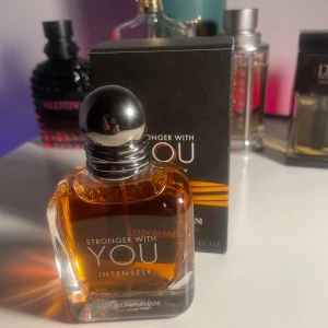Stronger With You Intensely  - Säljer en flaska av parfymen Stronger With You Intensely från Emporio Armani. Flaskan har en elegant design med en rundad metallkork och en djup bärnstensfärgad vätska. Förpackningen är svart med orange detaljer och text i vitt. Perfekt för den som vill ha en intensiv och kraftfull doft. Endast testad!