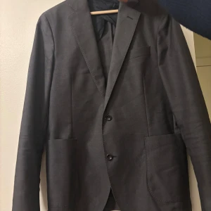 Grå kavaj från Oscar Jacobson - Snygg grå kavaj från Oscar Jacobson. Perfekt för en stilren look med två knappar framtill och klassisk passform. Passar utmärkt till både formella och semi-formella tillfällen. Passar M men även L ifall inte så bredaxlad. 