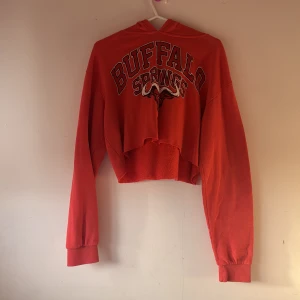 Röd croppad hoodie med tryck - Säljer en röd croppad hoodie med texten 'Buffalo Springs' tryckt på framsidan. Hoodien har långa ärmar och en bekväm huva. Perfekt för en avslappnad stil.