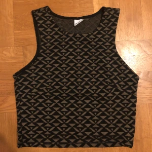 Svart och grå ärmlös topp med geometriskt mönster - Ärmlös topp i svart och khaki grön med ett geometriskt mönster. Perfekt för att ge din outfit en modern touch. Passform:tight form. Kan även hämtas på plats(T-centralen/Slussen)