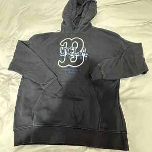 Mörkblå Oversize hoodie från H&M med UCLA-tryck - Säljer en mörkblå Oversize hoodie från H&M med stort UCLA-tryck på framsidan. Tröjan har en klassisk känguruficka och en justerbar huva med dragsko. Perfekt för en avslappnad stil.