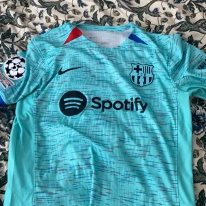Fc barcelona tröja  - Säljer en turkos fotbollströja från Nike med korta ärmar och tryck av Spotify-logga. Tröjan har även ett klubbmärke på bröstet och spelarnamnet 'Pedri' med nummer 8 på ryggen! Inget fel på tröjan den är perfekt 