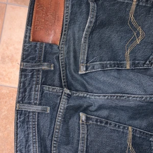Mörkblå jeans från Replay - Snygga mörkblå jeans från Replay i modellen Grover. Klassisk femficksdesign med knappgylf och läderdetalj vid midjan. Perfekta för en avslappnad stil.
