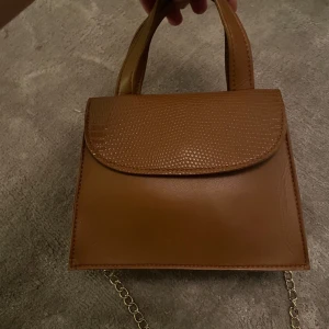 Brun handväska från Koton - Snygg brun handväska i skinn från Koton med en elegant kedja som axelrem. Väskan är köpt utomlands. Nytt skick och har använts två gånger. Priset kan diskuteras! Frakt ingår ej