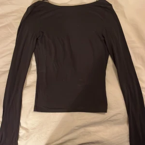 Svart långärmad topp med öppen rygg - Snygg svart långärmad topp med en djup öppen rygg. Perfekt för en stilren och elegant look. Passar bra till både jeans och kjol.