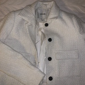 Vit jacka från Aware - Snygg vit jacka från Aware med knappar framtill och två fickor. Jackan har en stilren design och är perfekt för en elegant look. Har använt den endast EN gång, ny pris 700kr