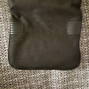 Svart axelväska från Hugo Boss - Snygg svart axelväska från Hugo Boss med justerbar rem. Väskan har en stilren design med subtil logotyp på framsidan. Perfekt för att bära dina dagliga nödvändigheter med stil.